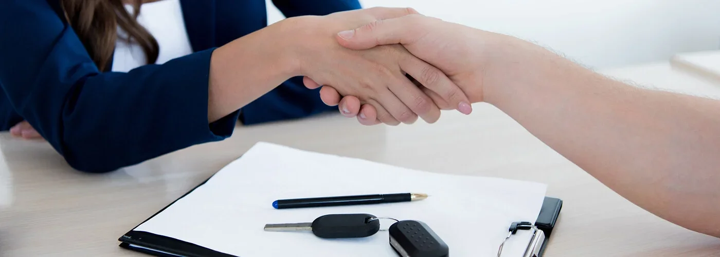 Two people shaking hands over a car key and a pen on a document.