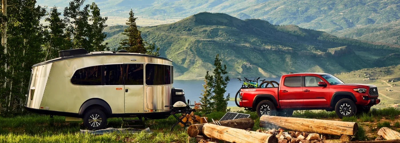 A red pickup truck with two bicycles in the bed, next to an Airstream trailer, overlooking a lake and mountains.
